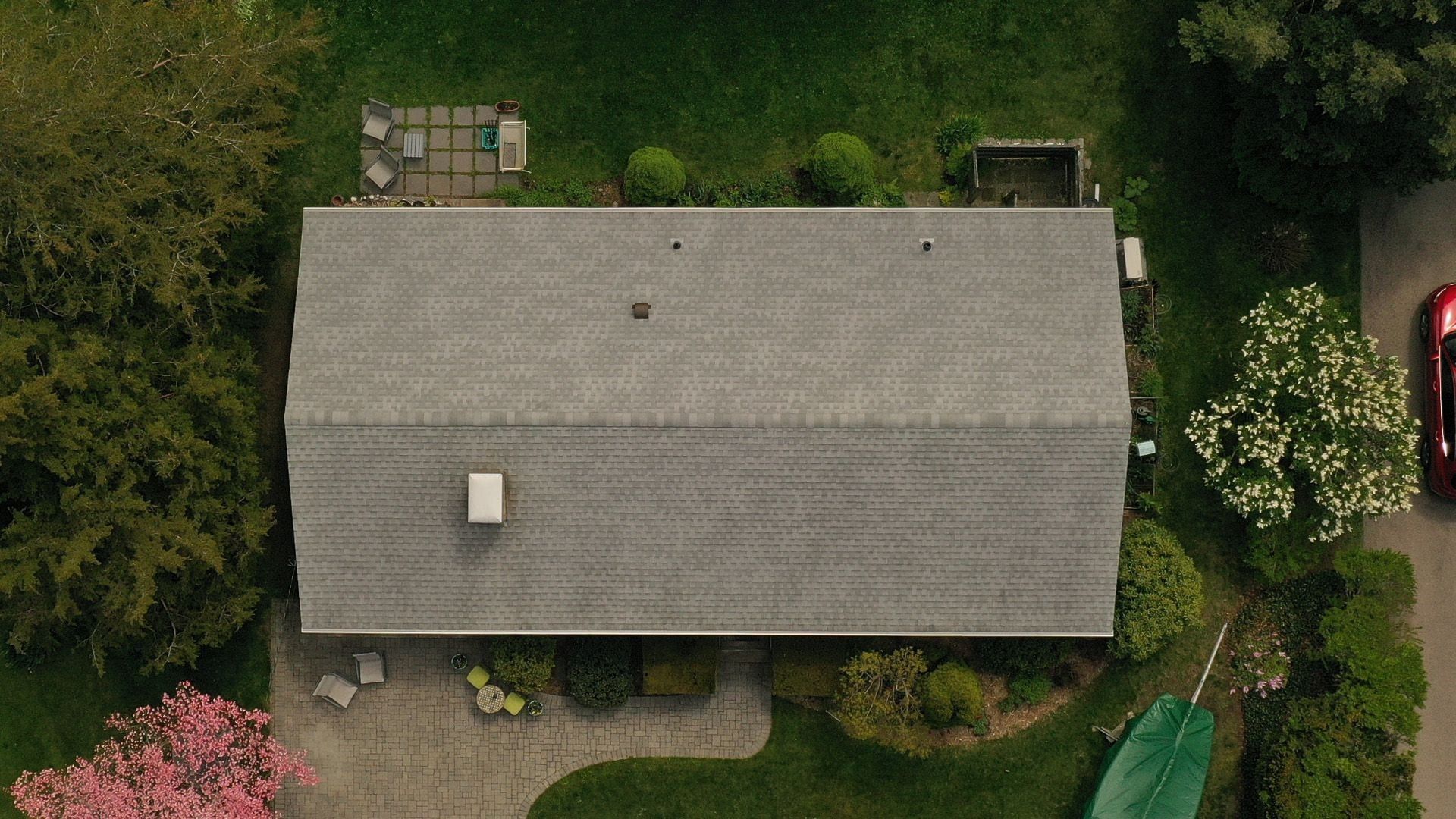Overhead view of a weathered grey gable roof beside a flowering tree.