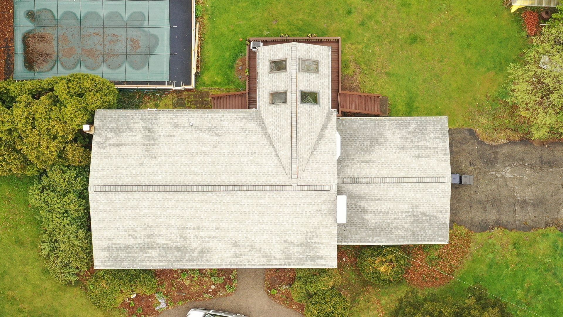 Overhead view of a mottled grey roof with four skylights on a projecting gable, pool cover below.