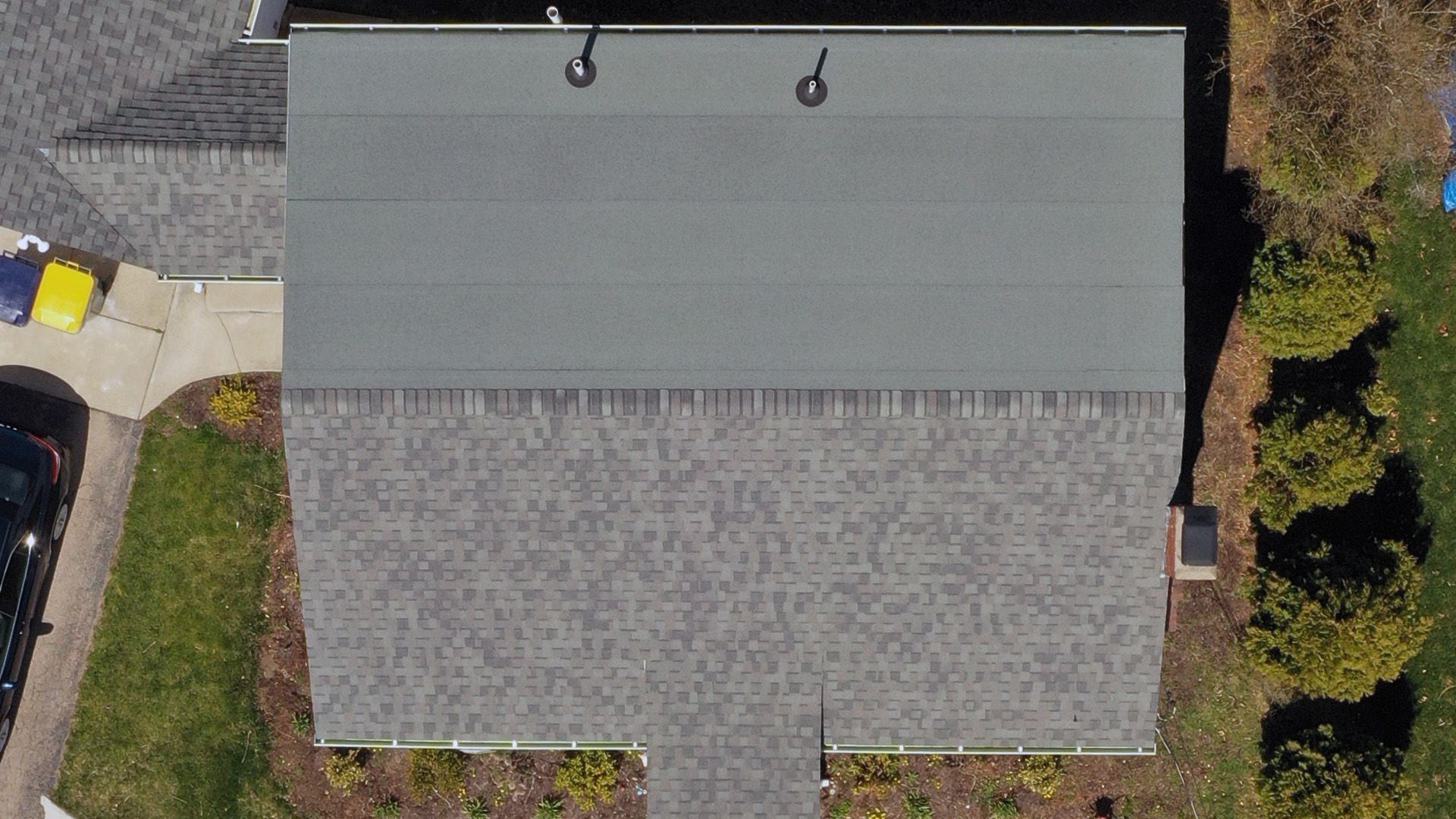 Close overhead view of a roof with green-grey roll roofing above grey architectural shingle.