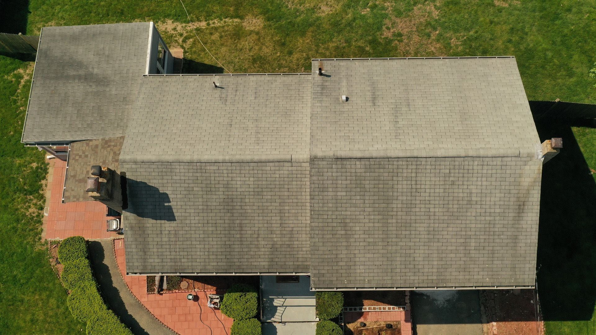 Overhead view of a streaked grey gable roof over a brick patio.