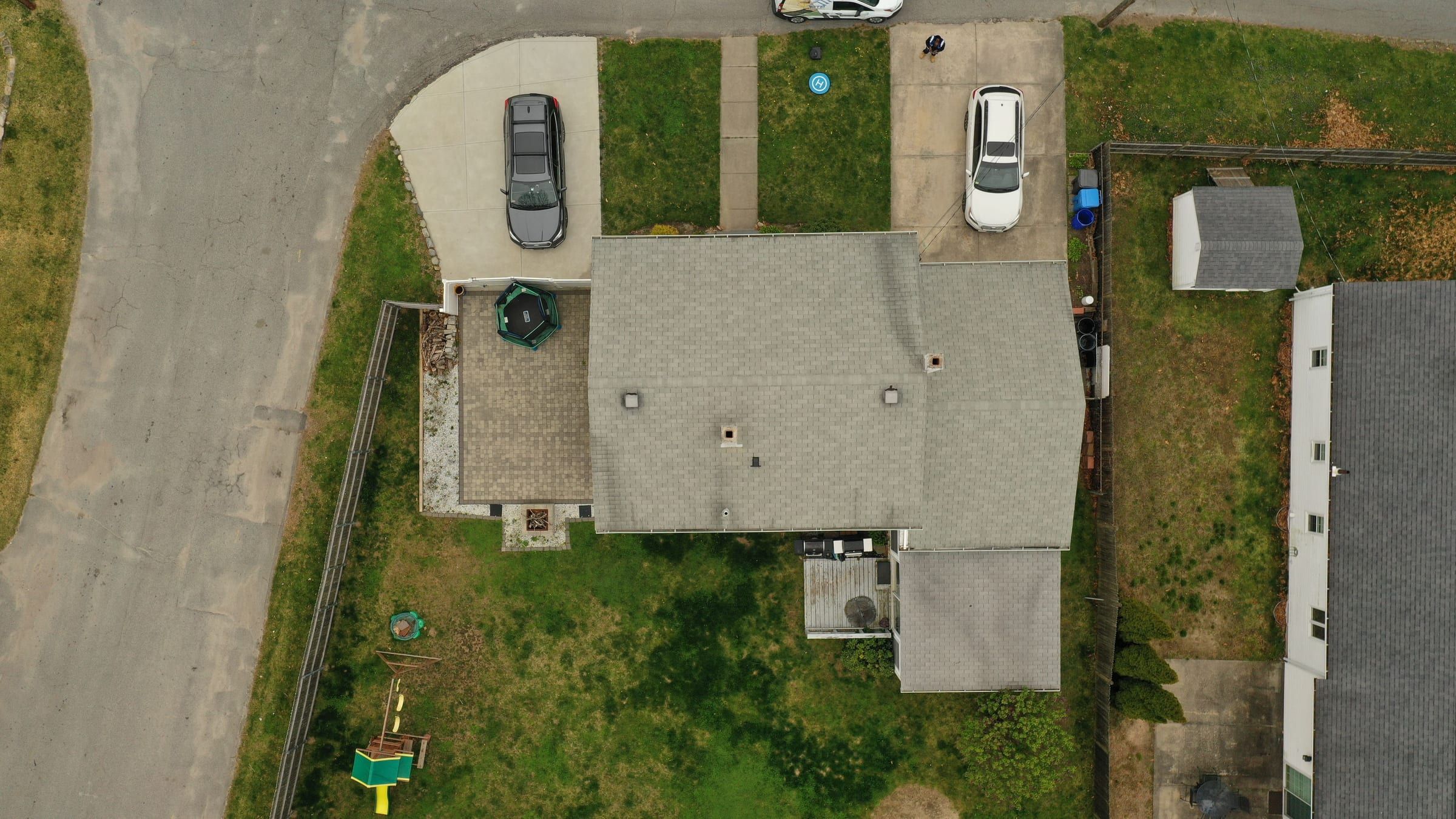 Wide drone view of a streaked grey roof, trampoline and neighbouring roofs.
