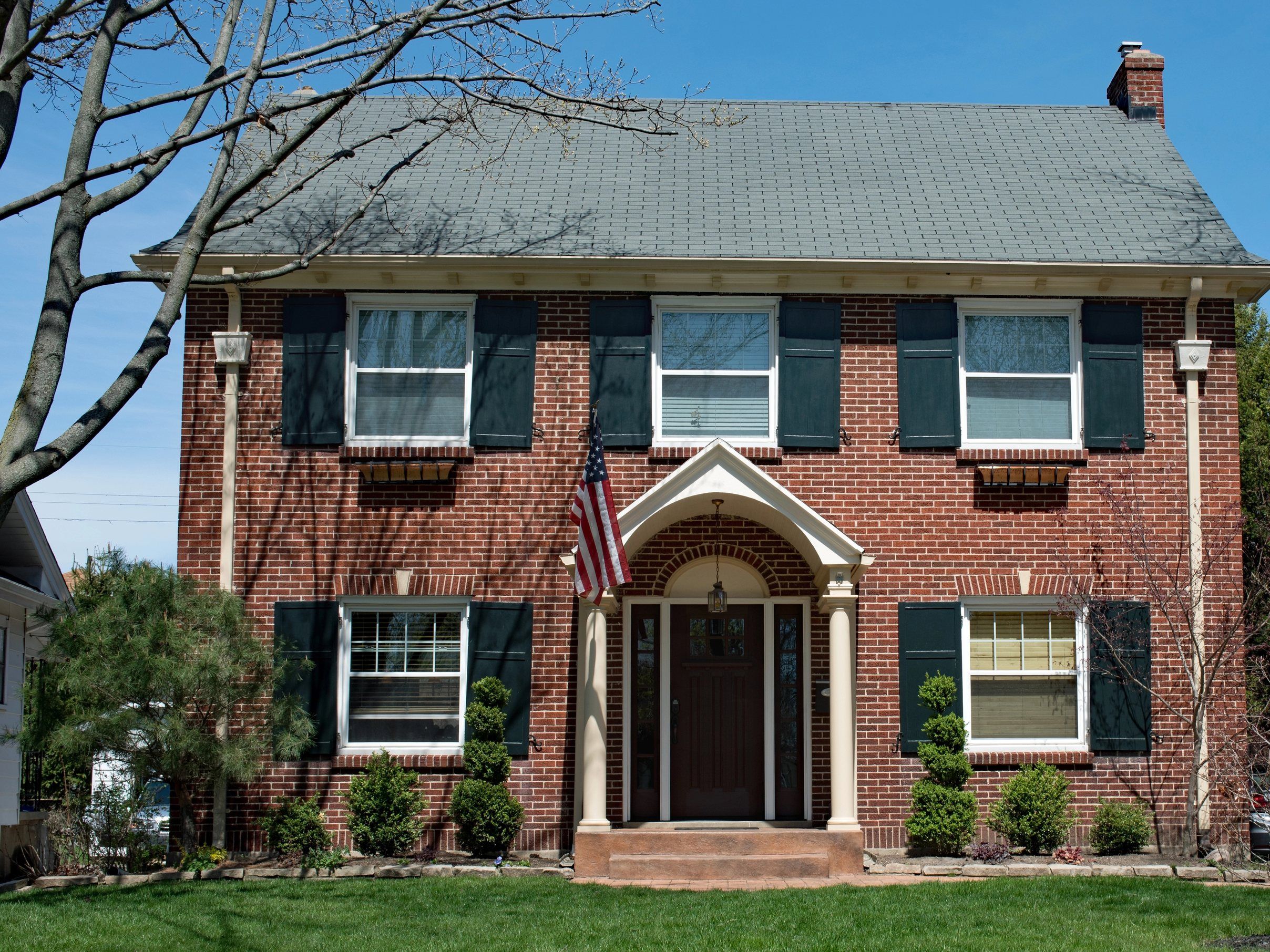 A red brick colonial with green shutters and a grey shingle roof.