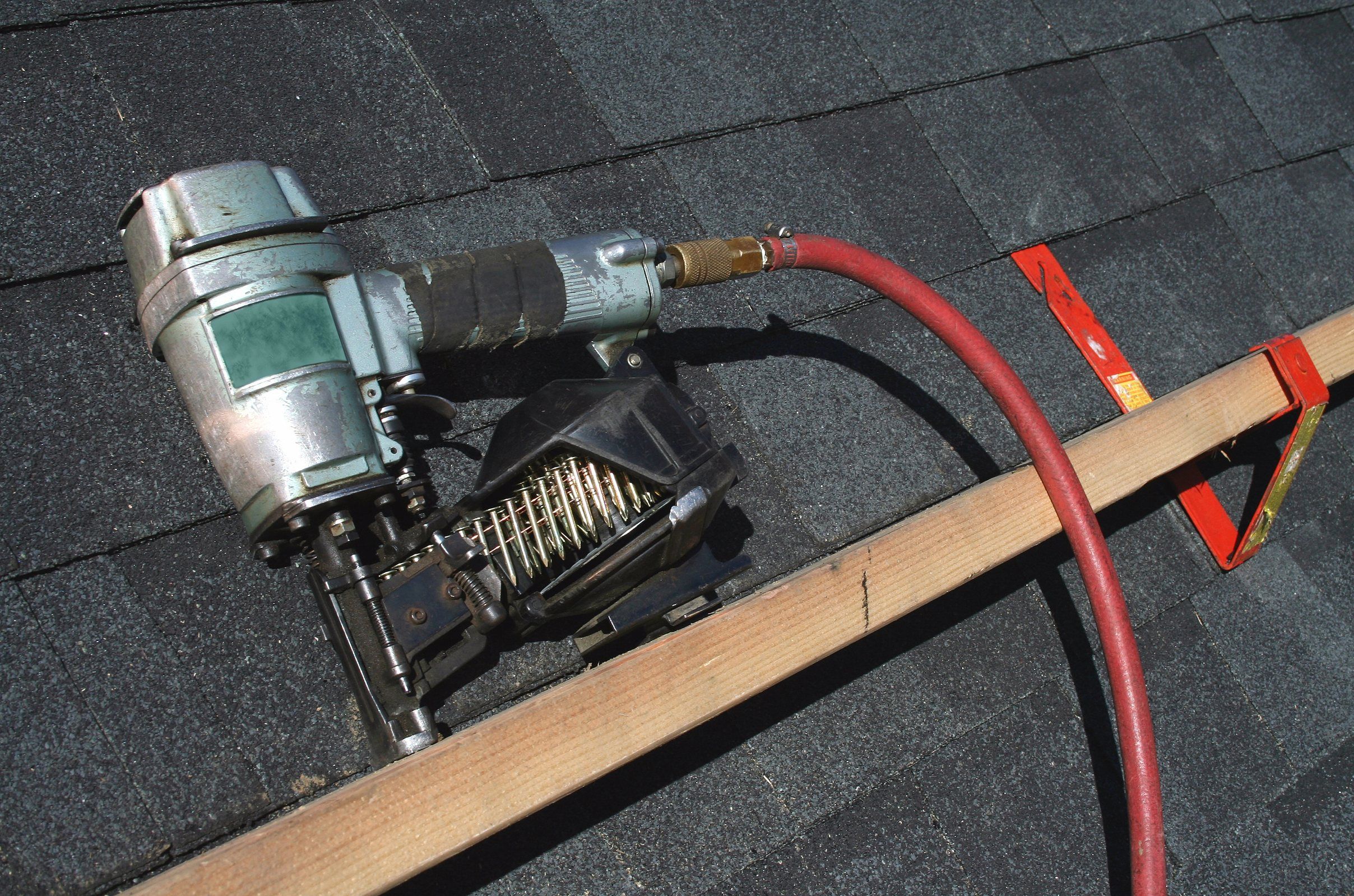 A coil roofing nailer and an air hose on a dark shingle roof.
