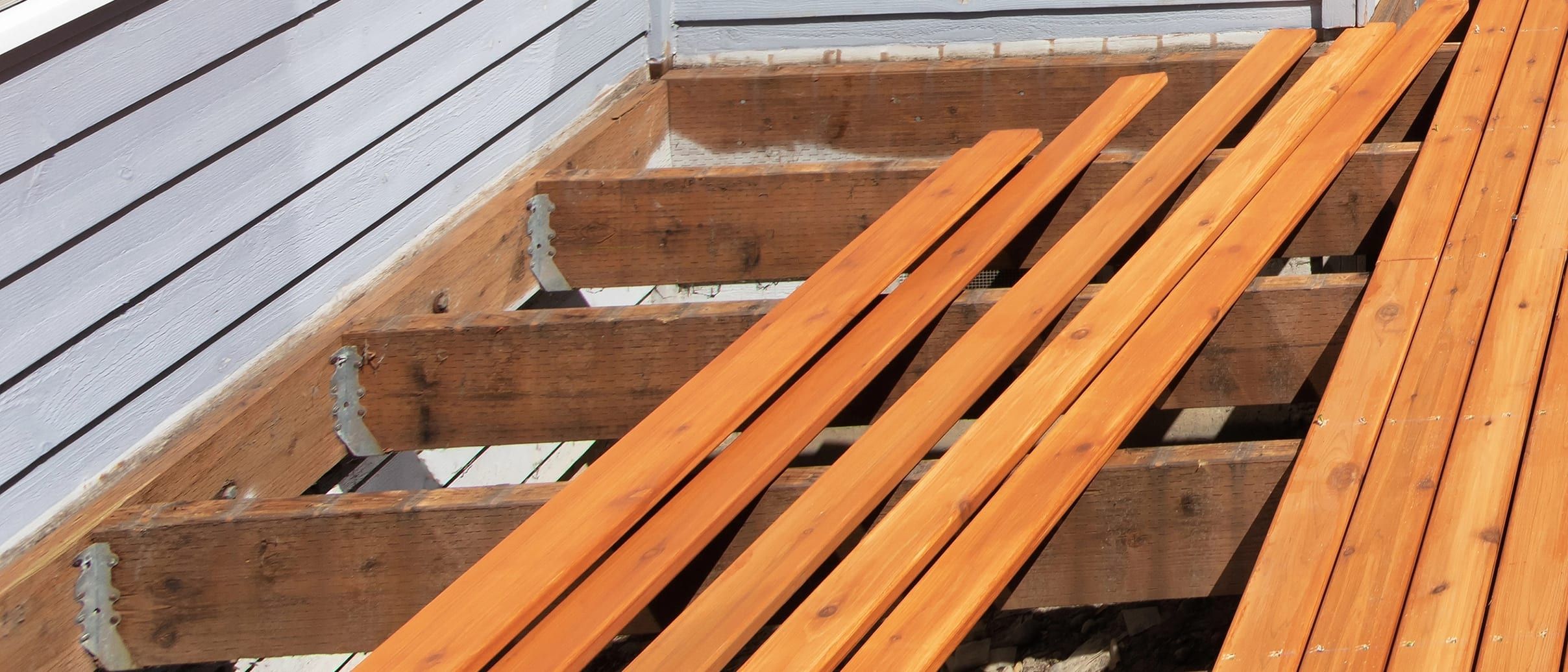 New cedar deck boards laid over old joists and hangers beside grey board siding.