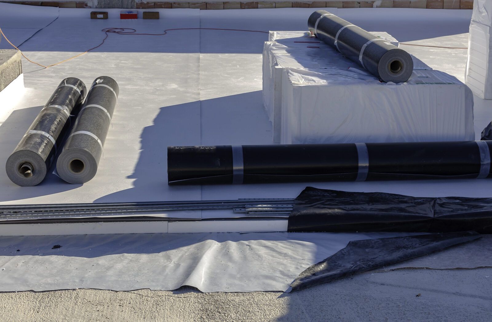 A white flat roof membrane with rolls of roofing material laid out on the roof.