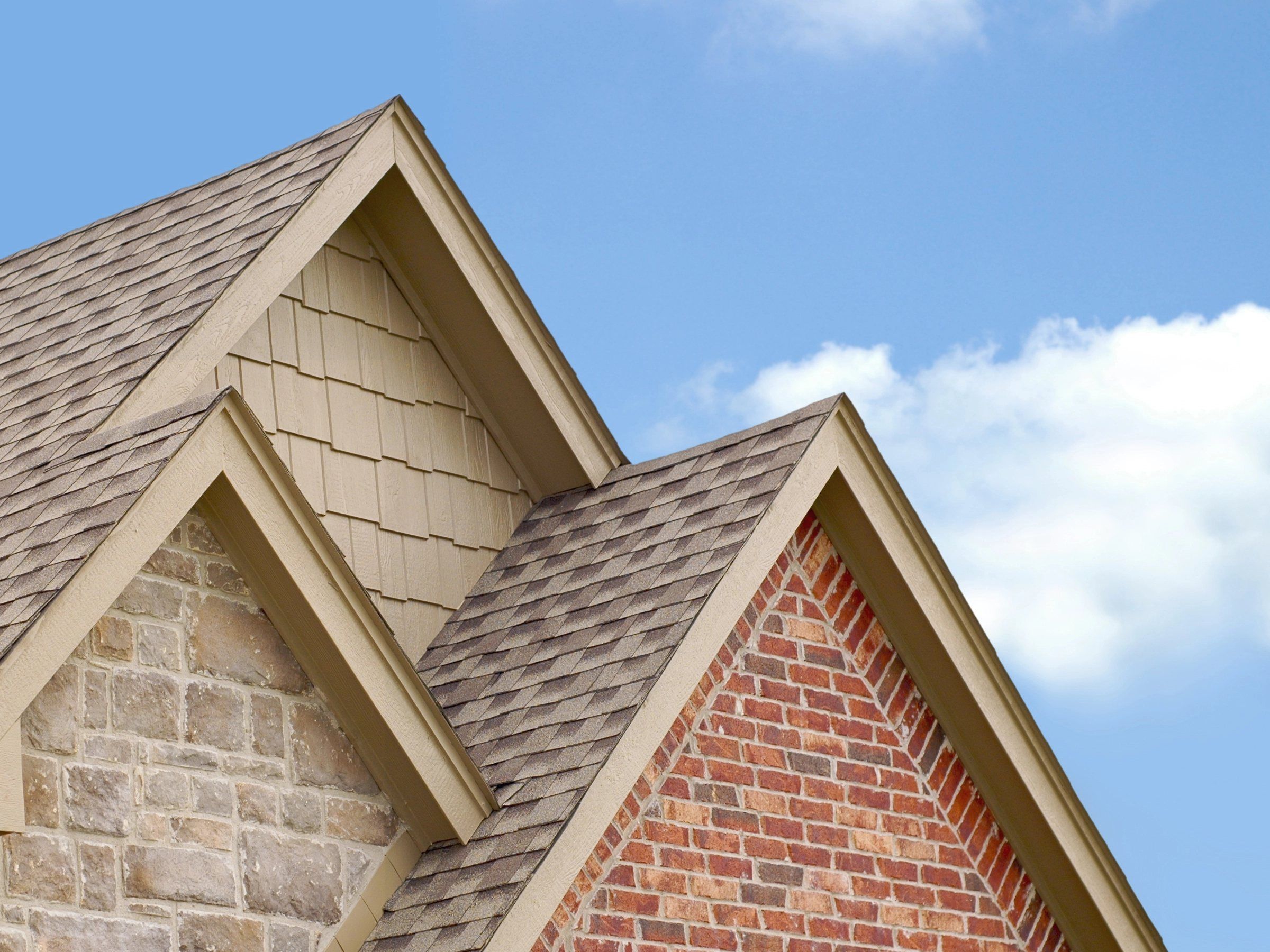Tan architectural shingles on two steep gables against a blue sky.