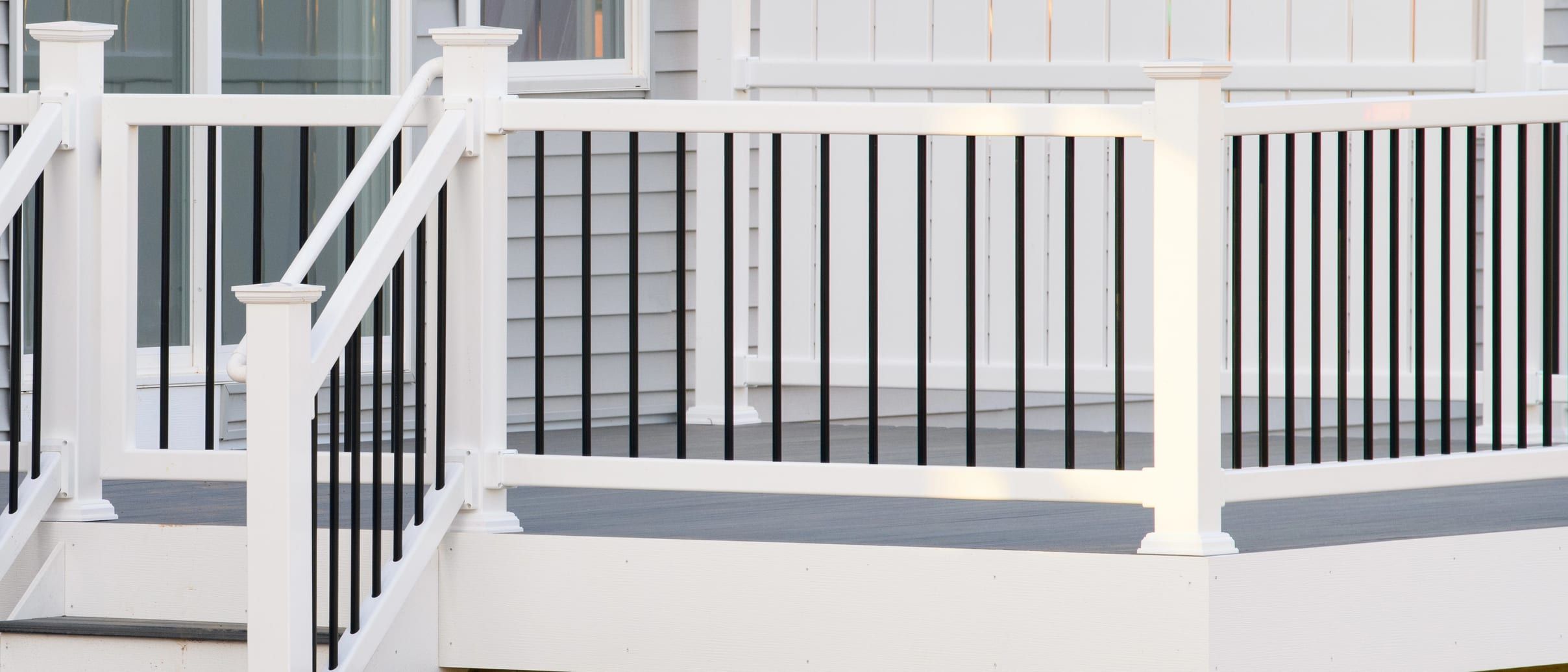 White composite deck with a grey board surface, white railing with black balusters and steps, beside a house with grey vinyl siding