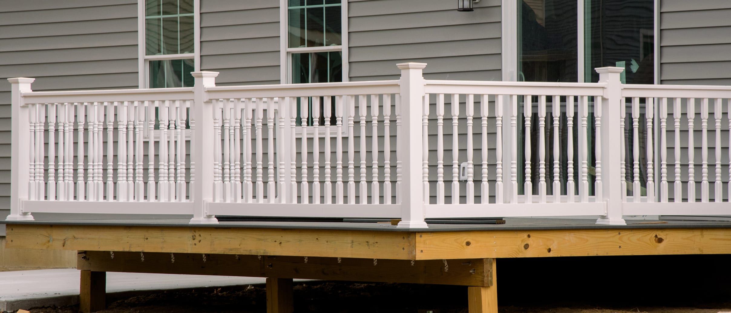 A new pressure-treated deck frame with a white railing against grey lap siding.