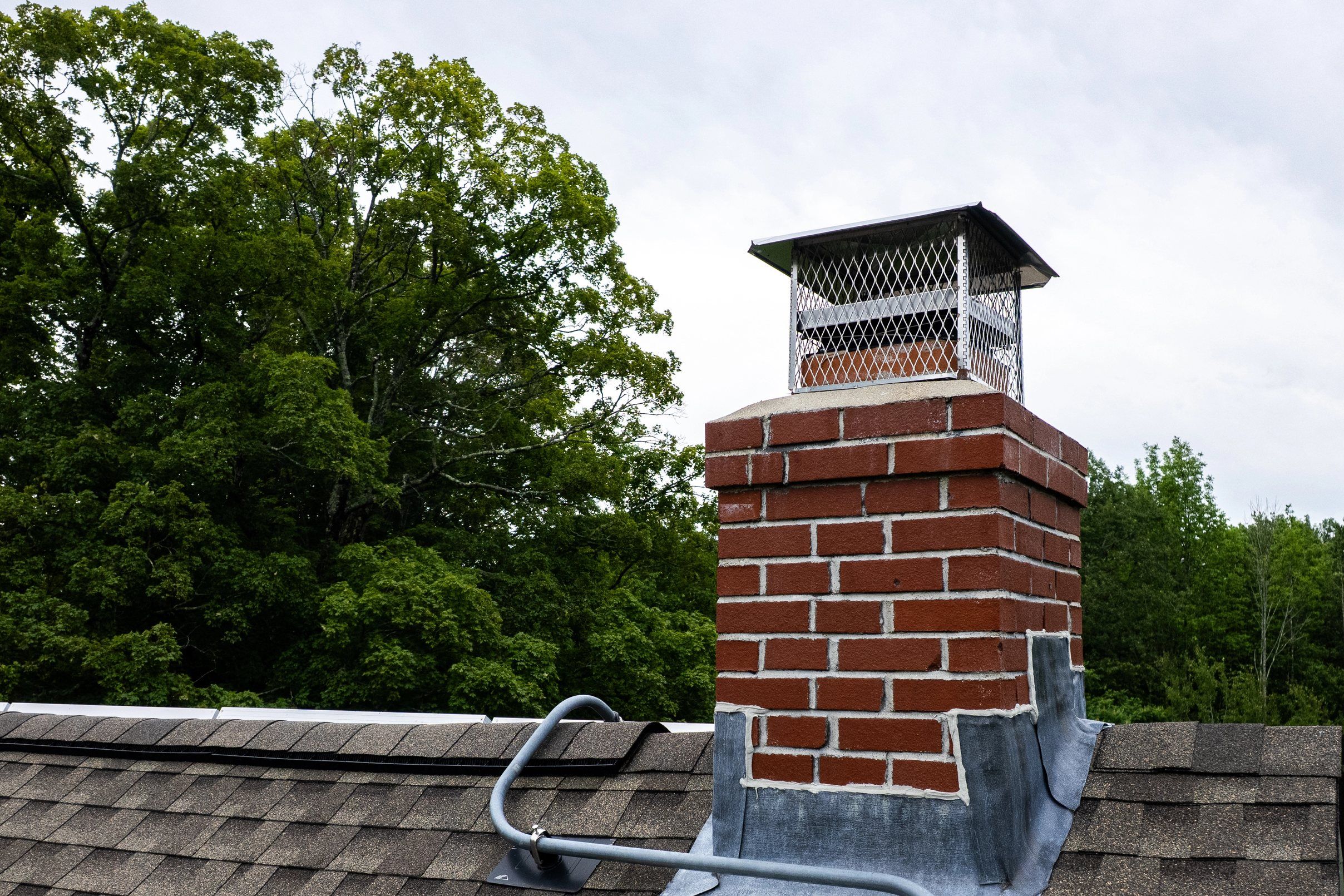 A brick chimney with a metal cap and new step flashing on a brown shingle roof.