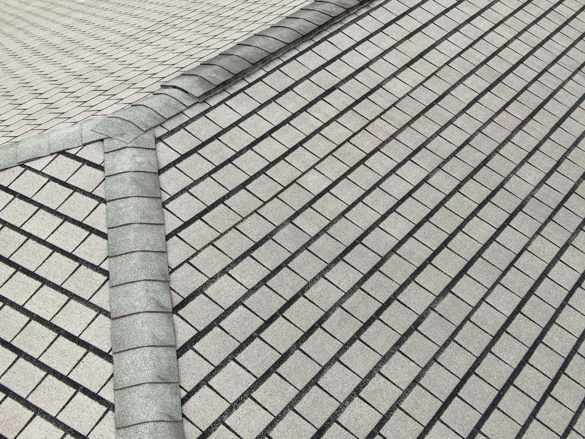 Grey shingles meeting under a ridge cap, seen from above.