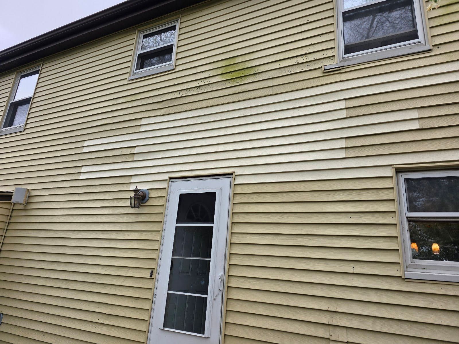 Yellow vinyl siding with a stained section and mismatched replacement panels beside a white door.