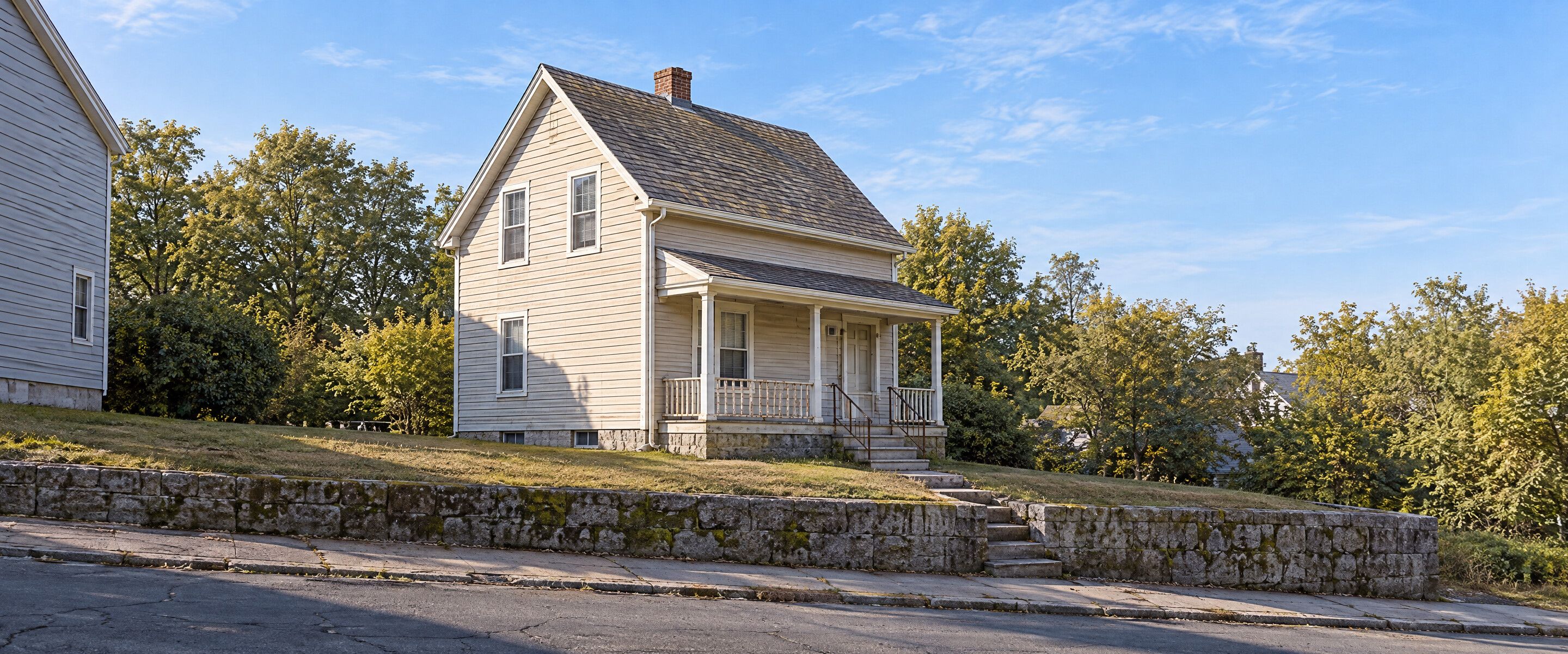 A row of older clapboard houses with grey shingle roofs on a quiet New England street at morning