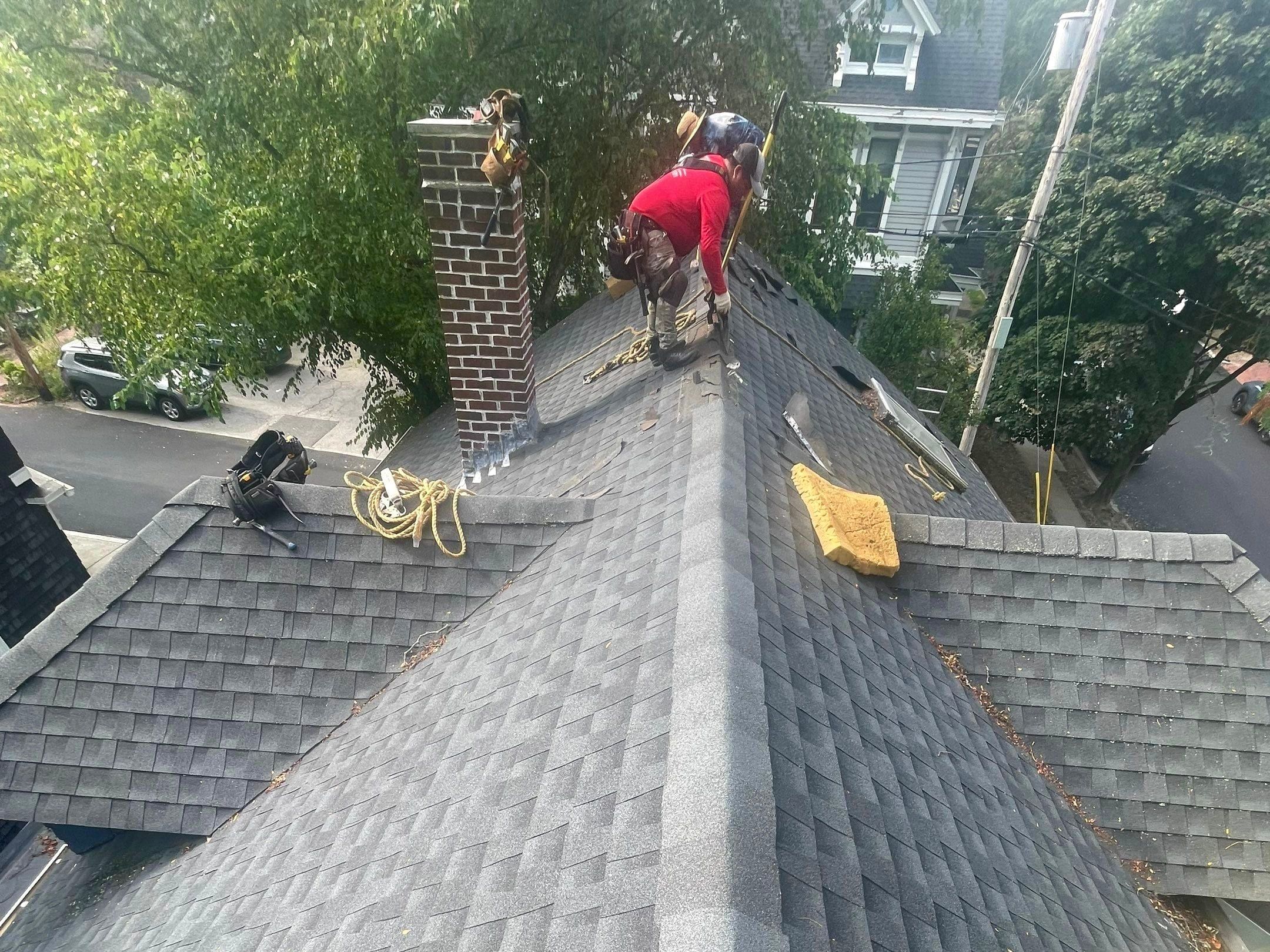 A roofer finishes the ridge beside a brick chimney with new flashing.