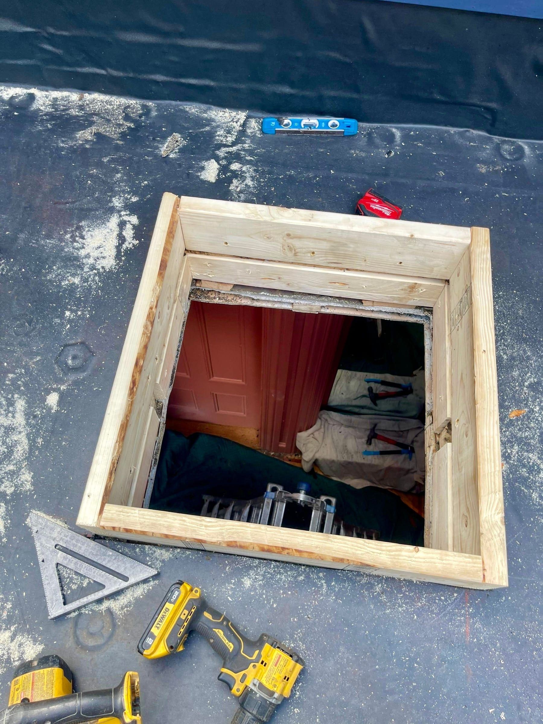 New lumber framing around a skylight opening in a black rubber low-slope roof, with hand tools beside it.