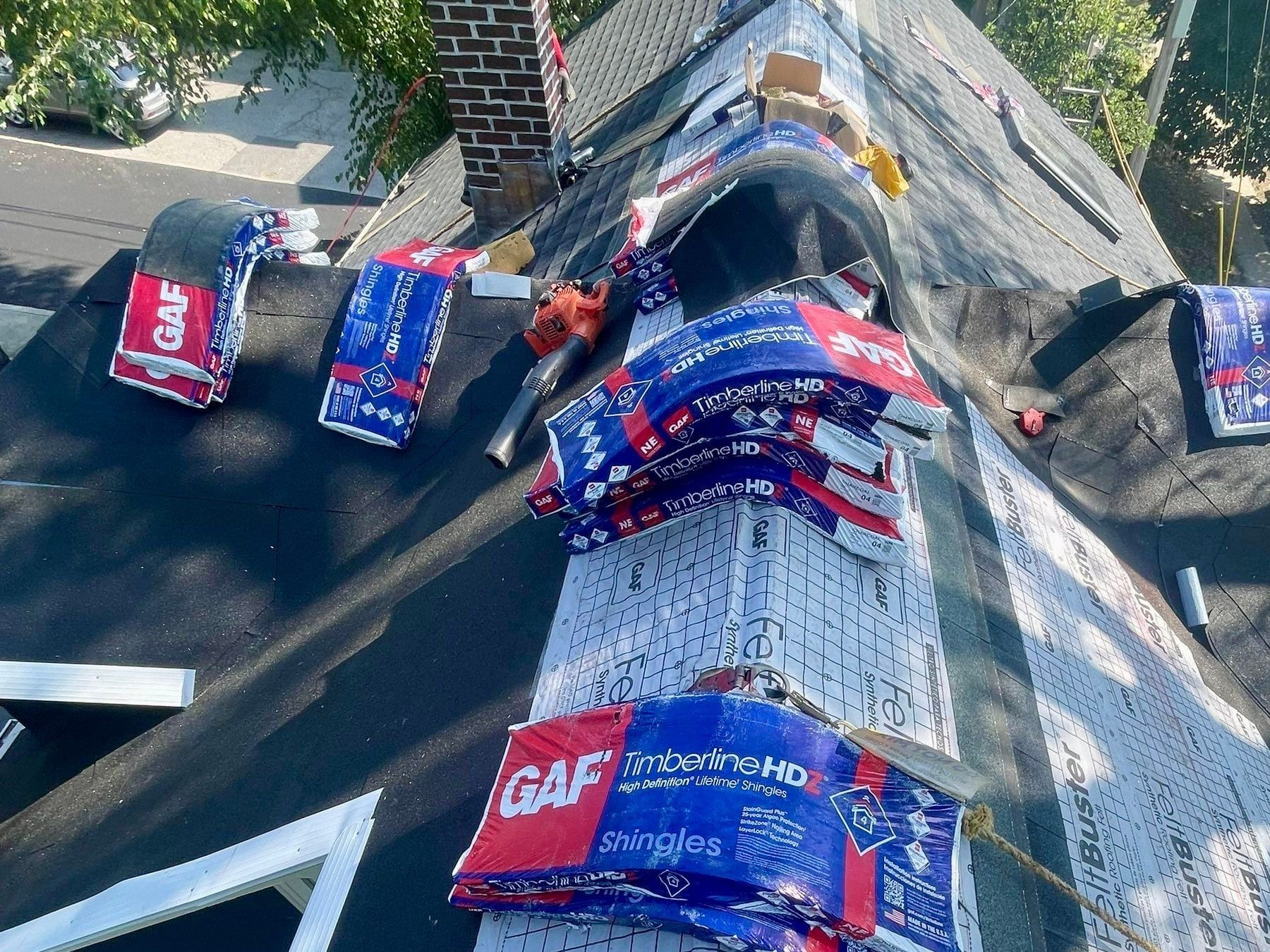 GAF Timberline HDZ shingle bundles staged along a ridge over synthetic underlayment beside a brick chimney.
