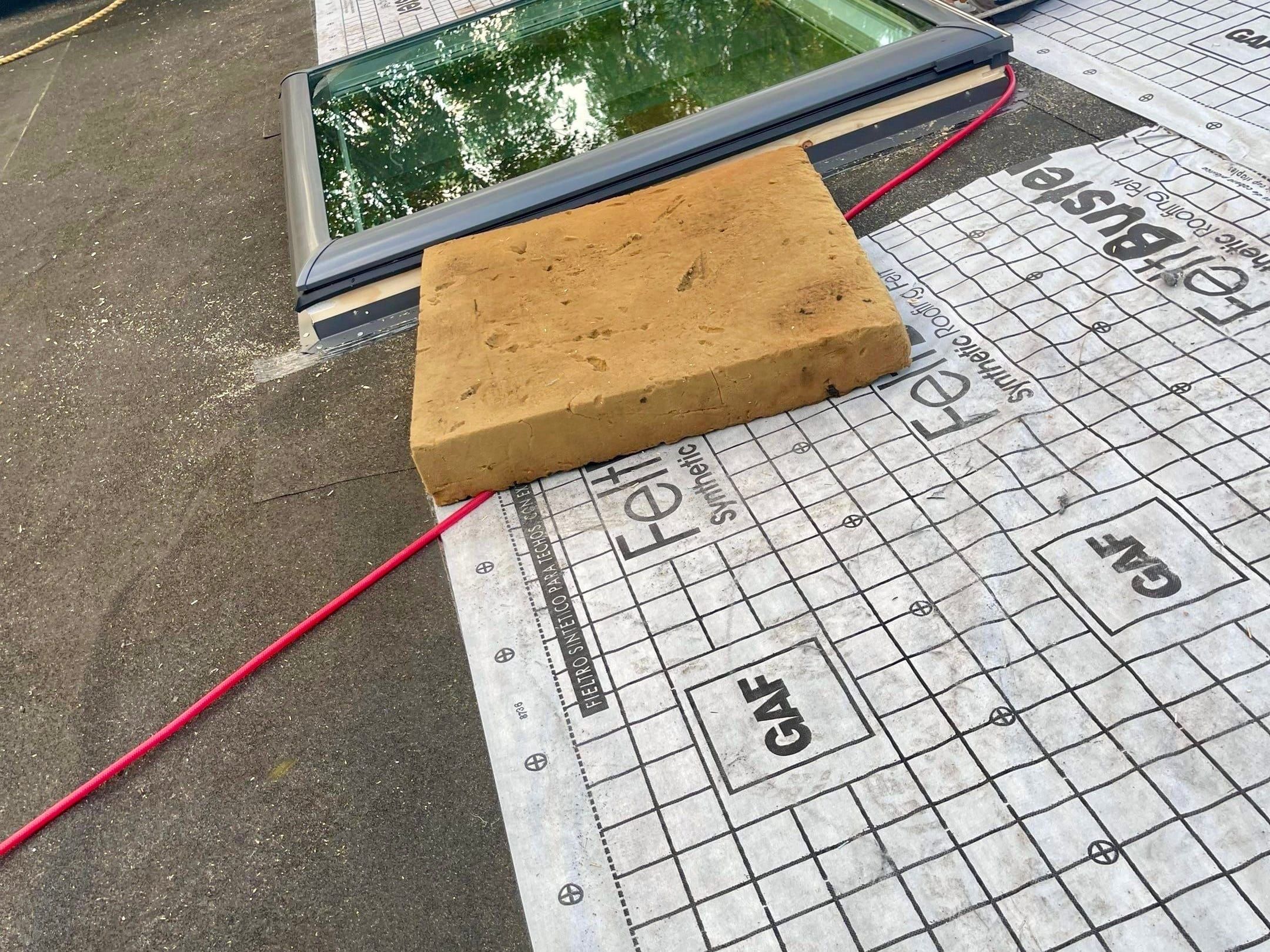 A new skylight set into a roof covered in GAF synthetic underlayment, a circular saw and air hose beside it.