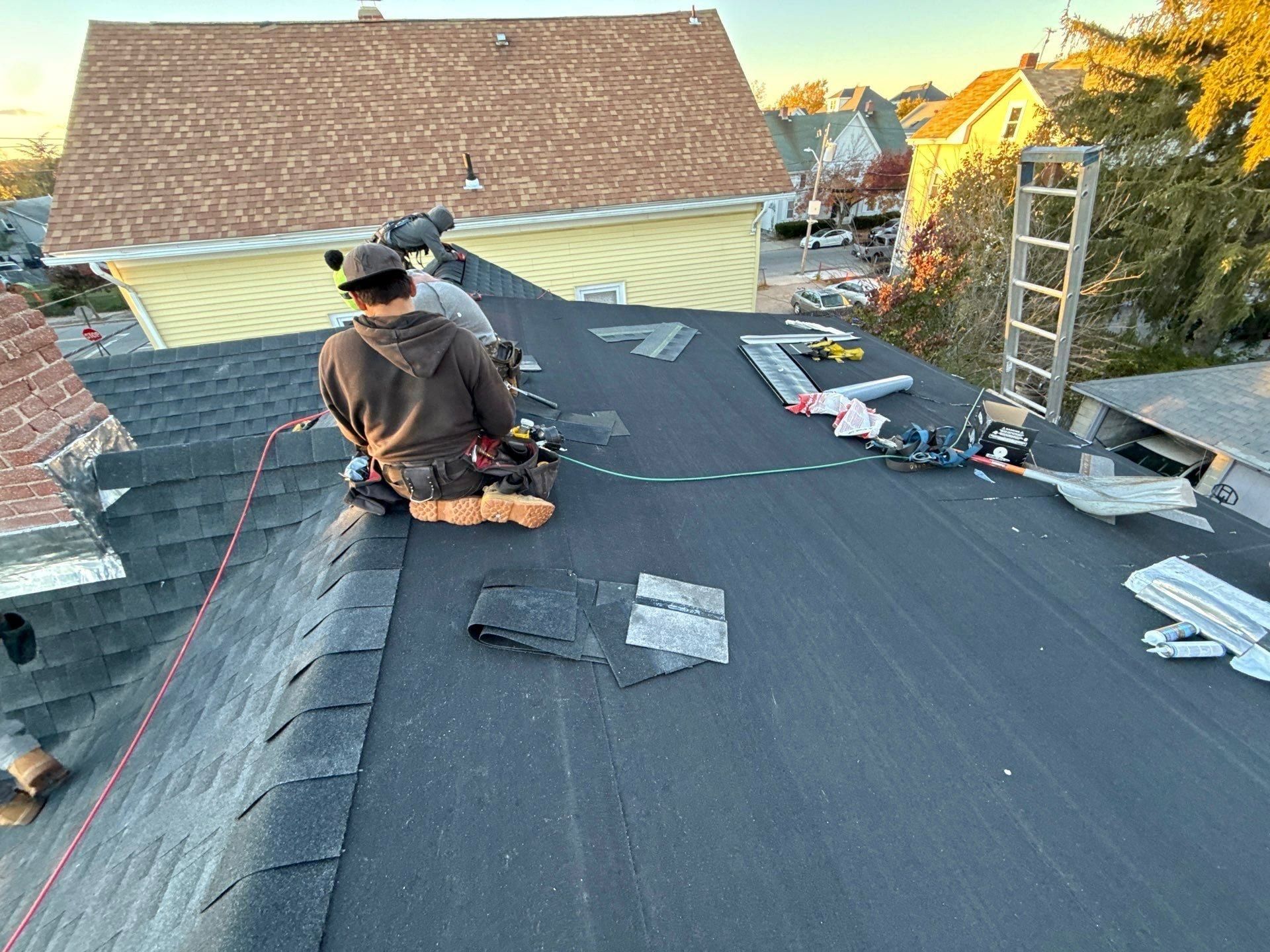 Three roofers finish a ridge at dusk on a roof with new underlayment, shingle scraps and tools around them.