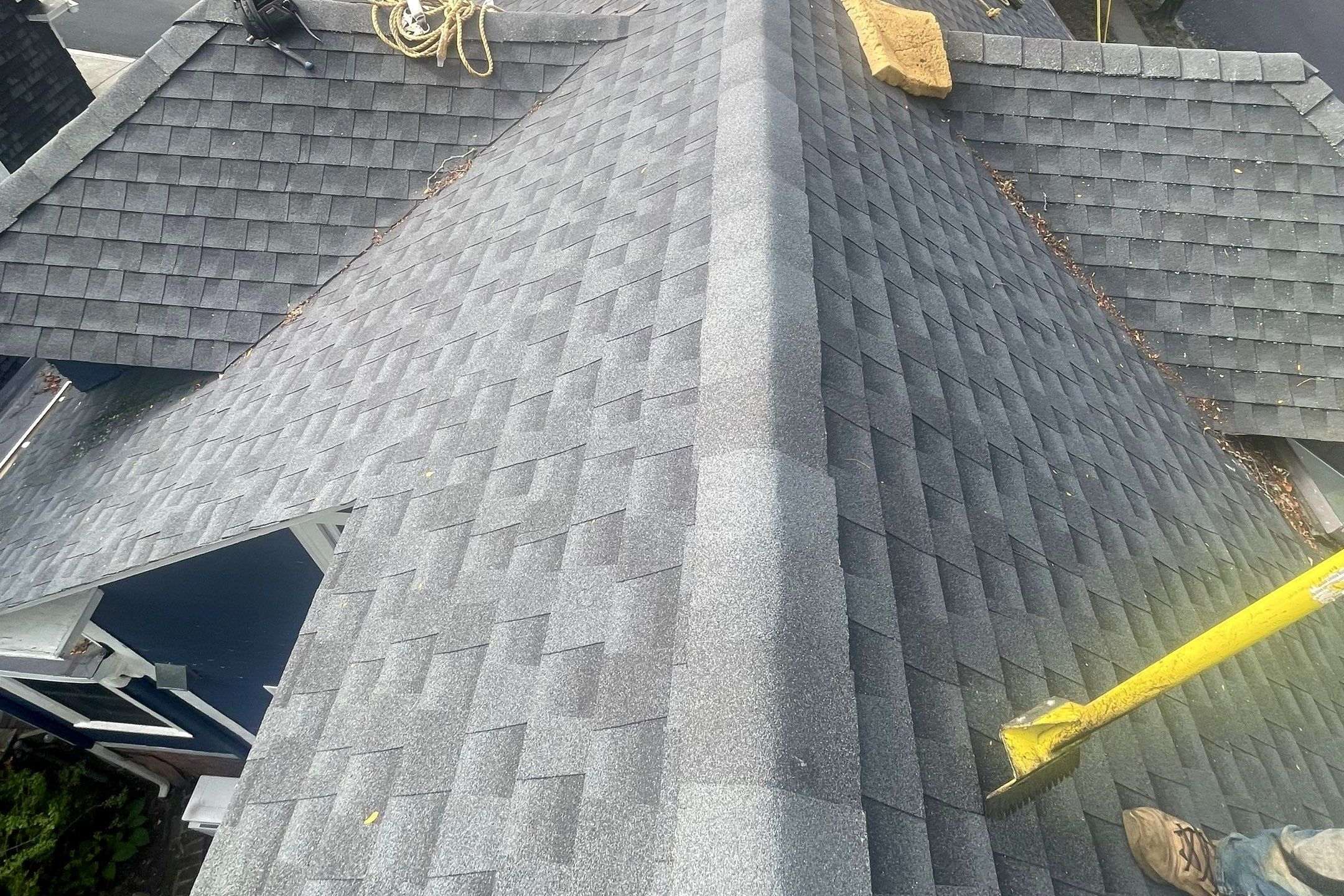 A new grey architectural-shingle hip roof with ridge cap, a rope and a shingle shovel left on it.